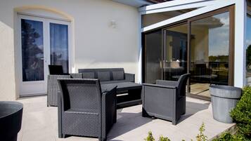 Une terrasse extérieure avec des meubles en osier, une porte-fenêtre coulissante et une plante en pot.
