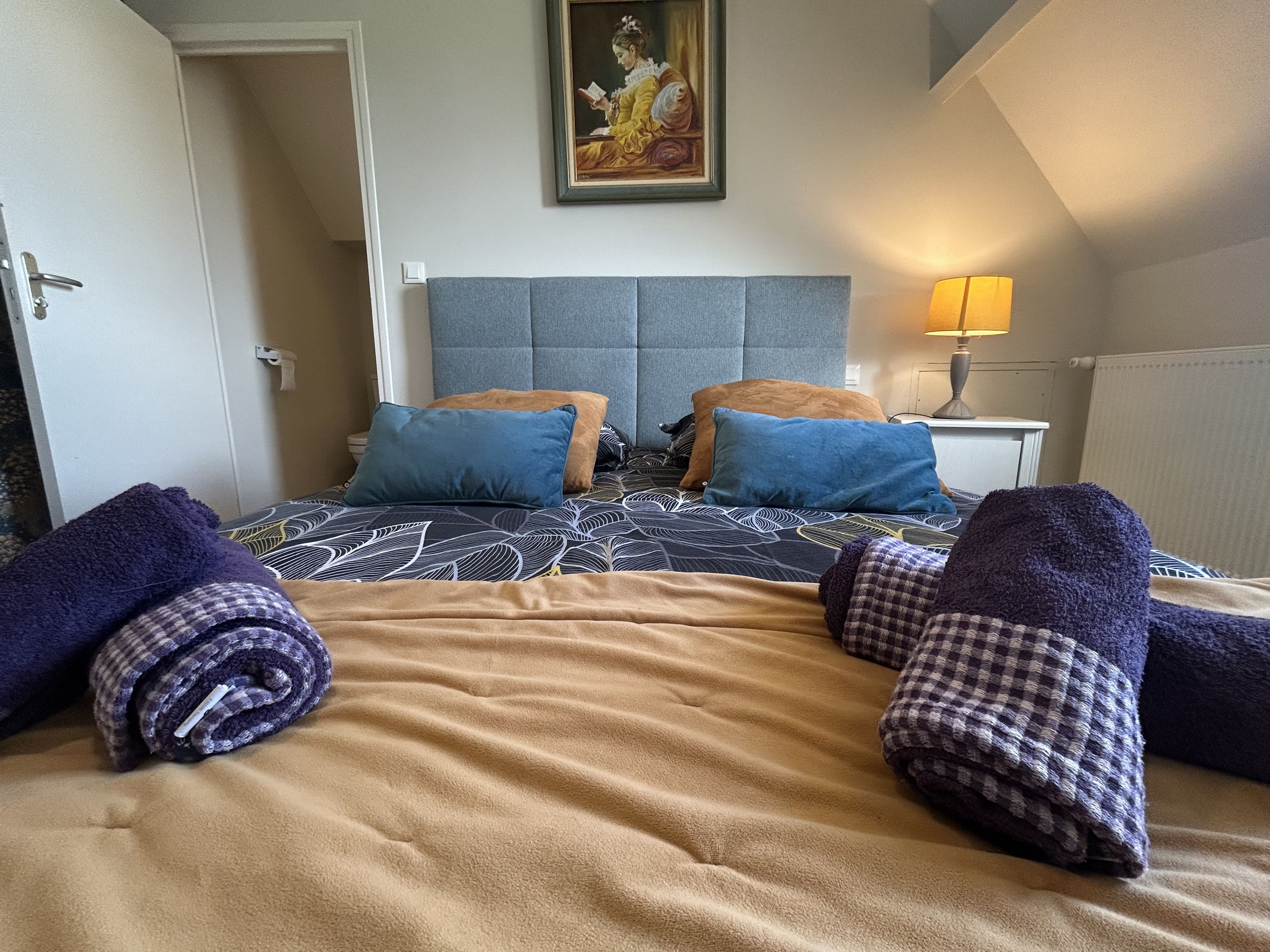 Une chambre d’hôtel avec un lit, des oreillers, un tableau au mur et une lampe.