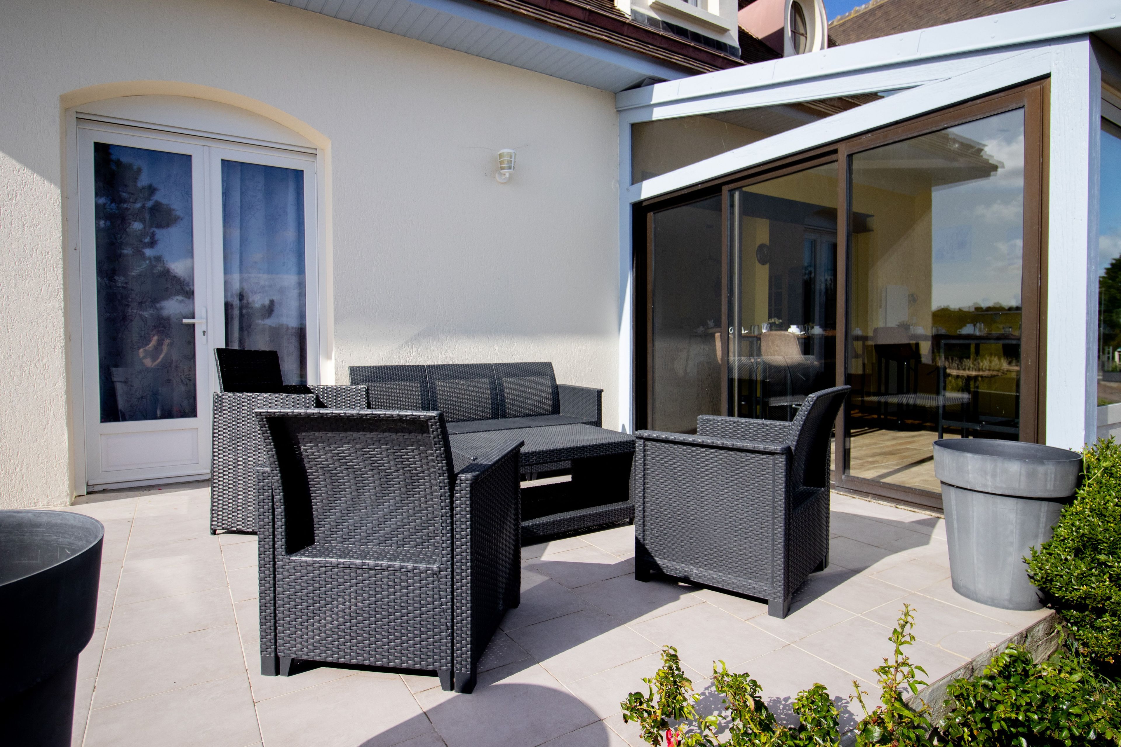 Un patio exterior con muebles de mimbre, un ventanal corredera y una planta en maceta.