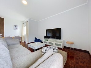 Een moderne woonkamer met een modulaire bank, een flatscreen televisie, een witte kast en een bijzettafeltje.
