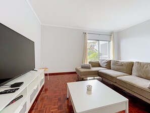 A modern living room with a flat-screen TV, a sofa, a coffee table, and a window with curtains. - Palmeira Apartment by Atlantic Holiday (Santa Cruz)