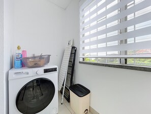 Een wasruimte met een wasmachine, een droogrek en een prullenbak.