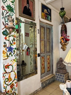 Une pièce avec une porte, un miroir, un luminaire fixé au mur et une petite statue.