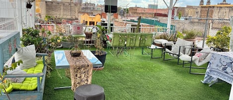 An outdoor patio with artificial grass, seating arrangements, and potted plants.