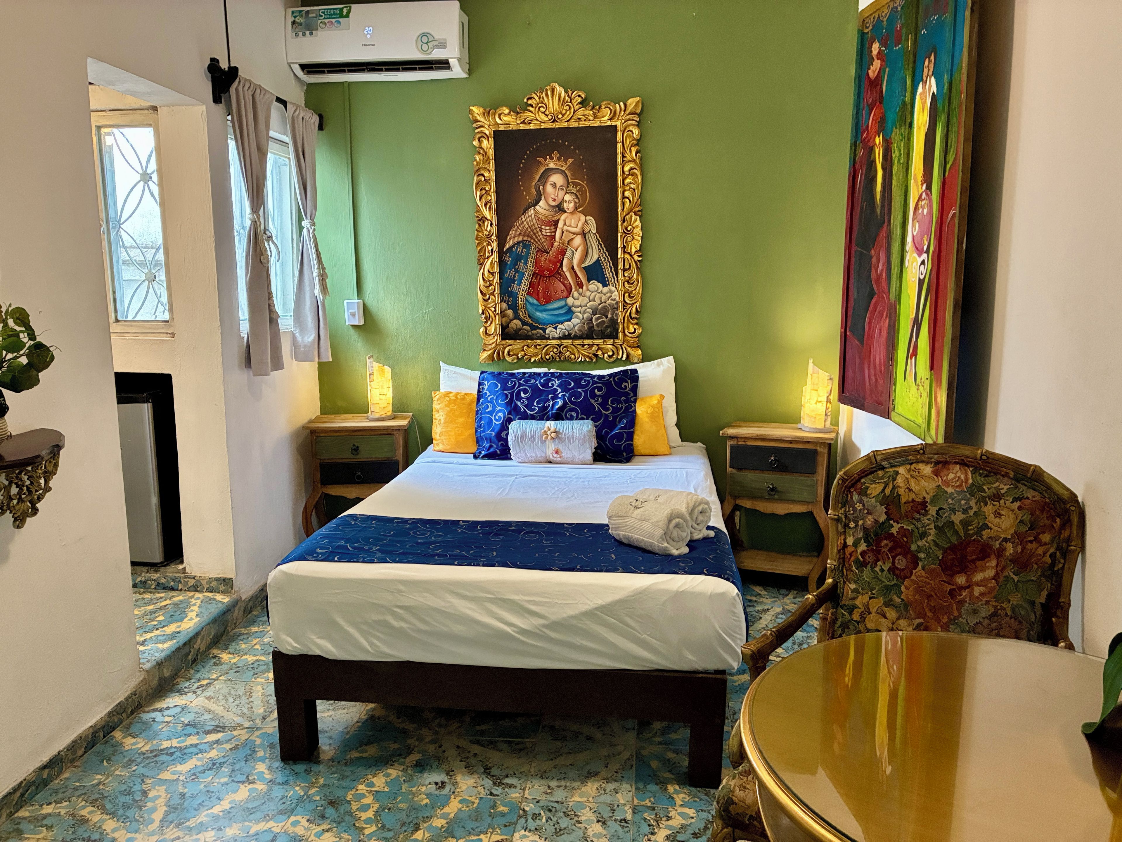Una habitación de hotel con cama, una silla, una mesa, un cuadro y un equipo de aire acondicionado.