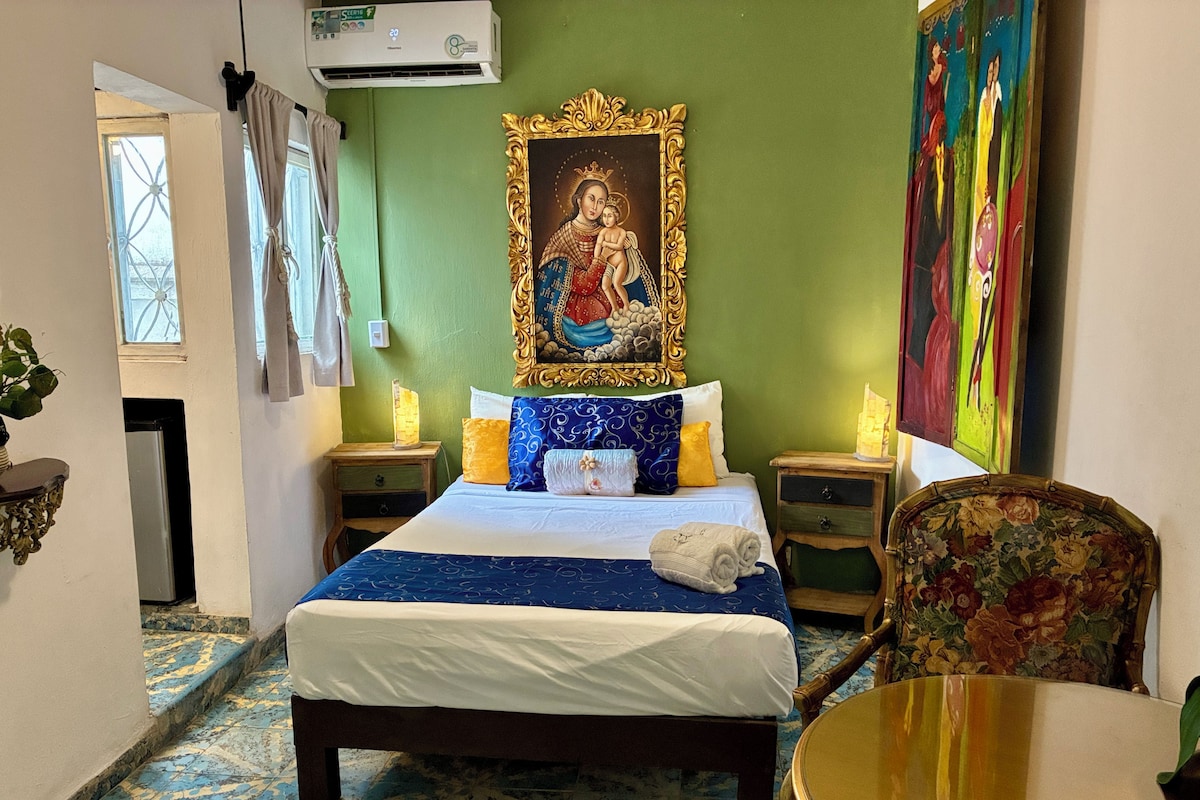 Een hotelkamer met een bed, een stoel, een tafel, een schilderij en een airconditioning.