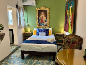Een hotelkamer met een bed, een stoel, een tafel, een schilderij en een airconditioning.
