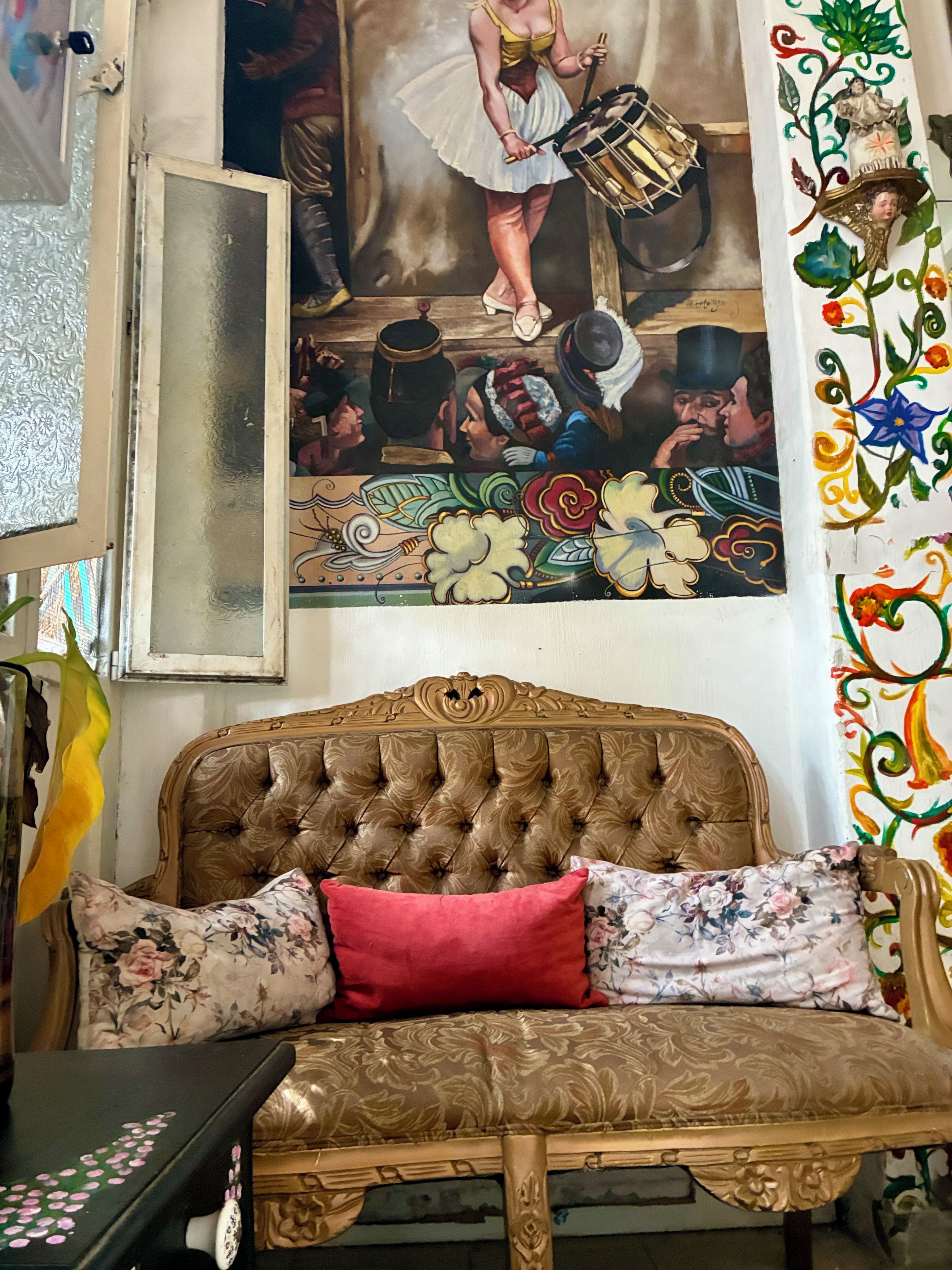 Una habitación con un sofá antiguo, una pared decorativa con un cuadro y una cortina estampada.