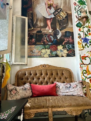 Une pièce avec un canapé de style vintage, un mur décoratif orné d’un tableau et un rideau à motifs.