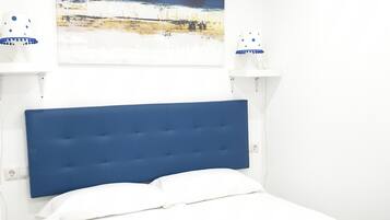 A bedroom with a bed, white walls, a blue headboard, and a painting above the bed.