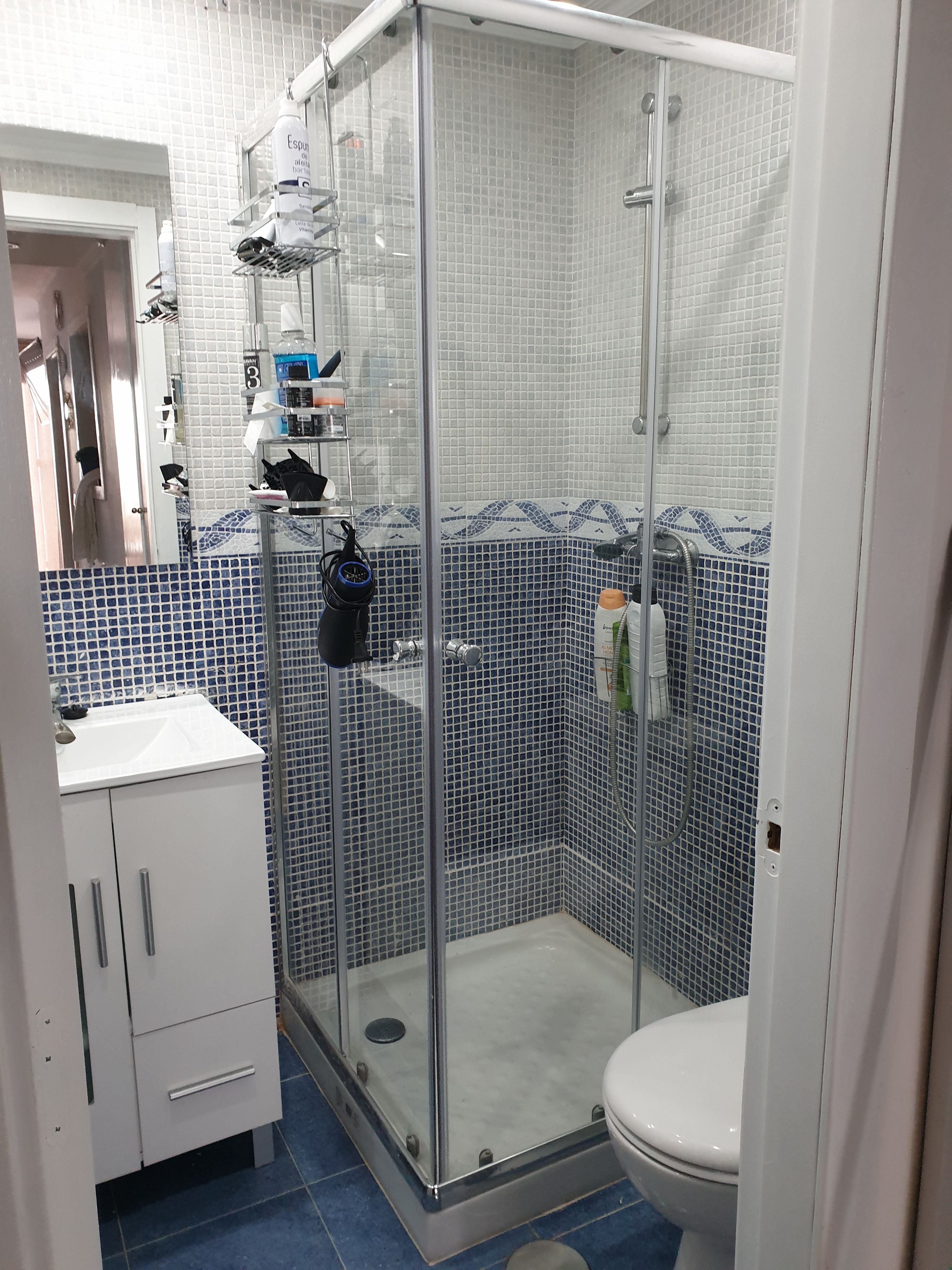 A bathroom with a glass-enclosed shower, white sink, and tiled walls.