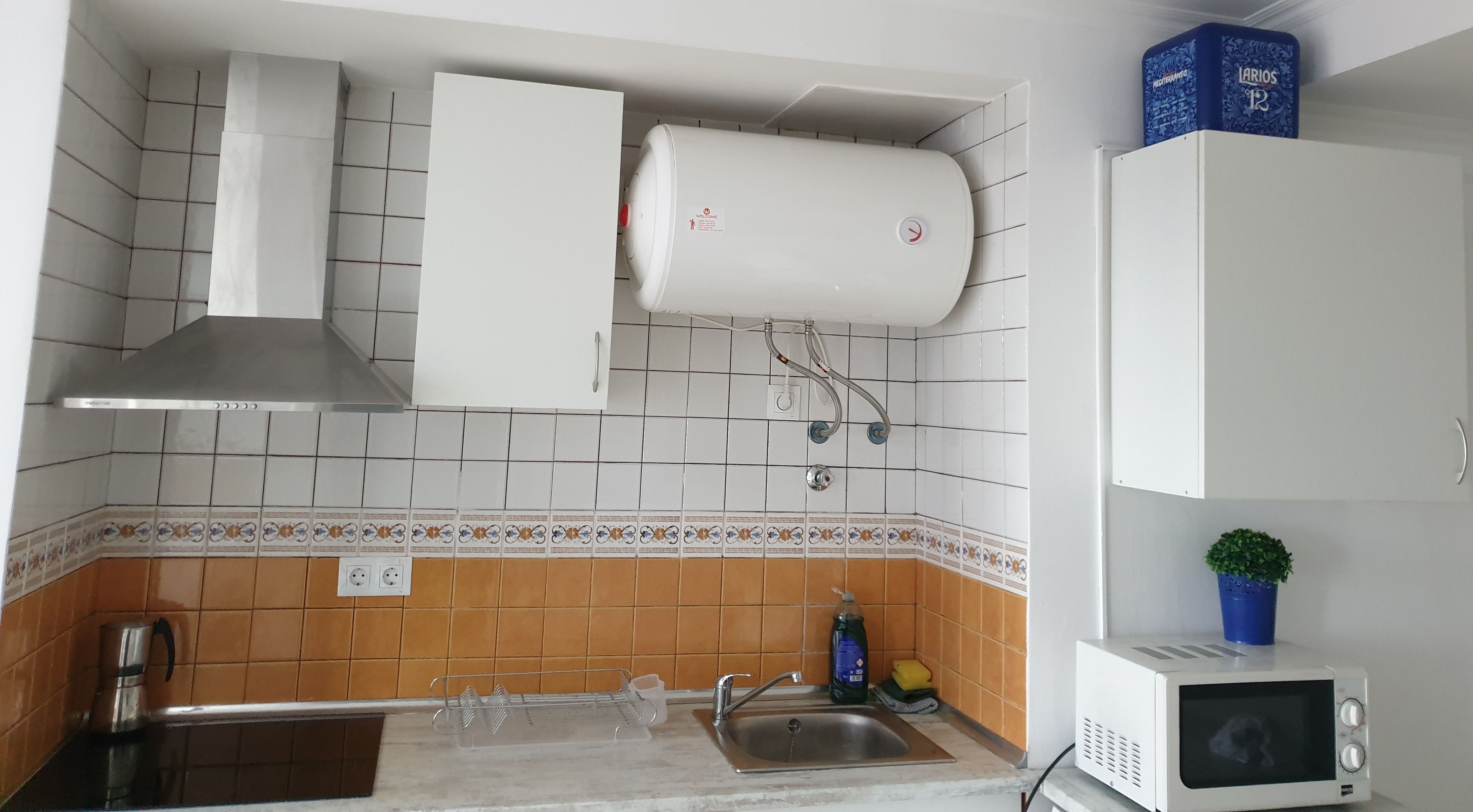 A kitchen with a sink, a microwave, a water heater, and a stove.