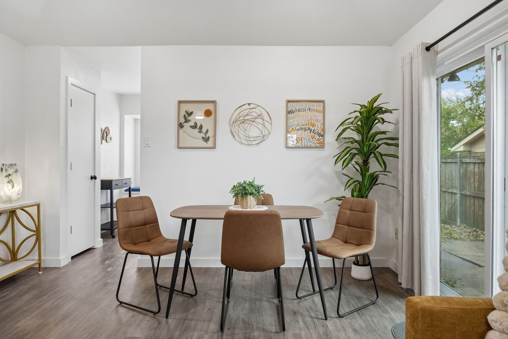 Spiseplads med et rundt bord, fire stole, en potteplante og billedkunst på væggen.