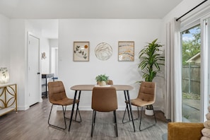 Spiseplads med et rundt bord, fire stole, en potteplante og billedkunst på væggen.