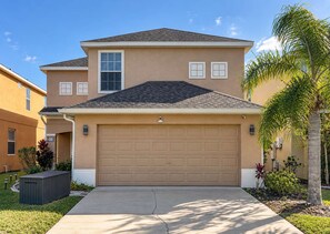 A two-story residential building with a garage, a small attached structure, and a palm tree. - Gated 4BR Oasis | Private Pool & Spa Near Disney (Kissimmee)