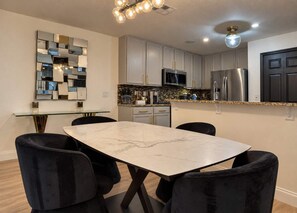 A modern kitchen with a marble countertop, stainless steel appliances, and a dining area with a glass table and black chairs. - Gated 4BR Oasis | Private Pool & Spa Near Disney (Kissimmee)