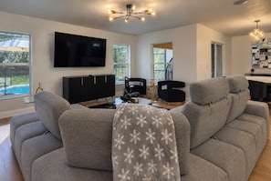 En moderne stue med en hjørnesofa, et fladskærms-tv og et spiseområde med et glasbord.
