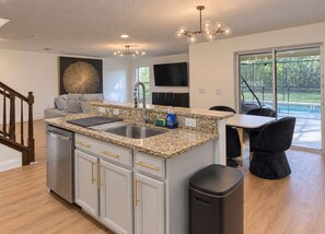 A modern kitchen with granite countertops, stainless steel appliances, and a black trash can. - Gated 4BR Oasis | Private Pool & Spa Near Disney (Kissimmee)