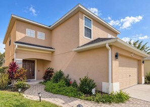 A two-story residential house with a garage, a front entrance, and a landscaped garden. - Gated 4BR Oasis | Private Pool & Spa Near Disney (Kissimmee)