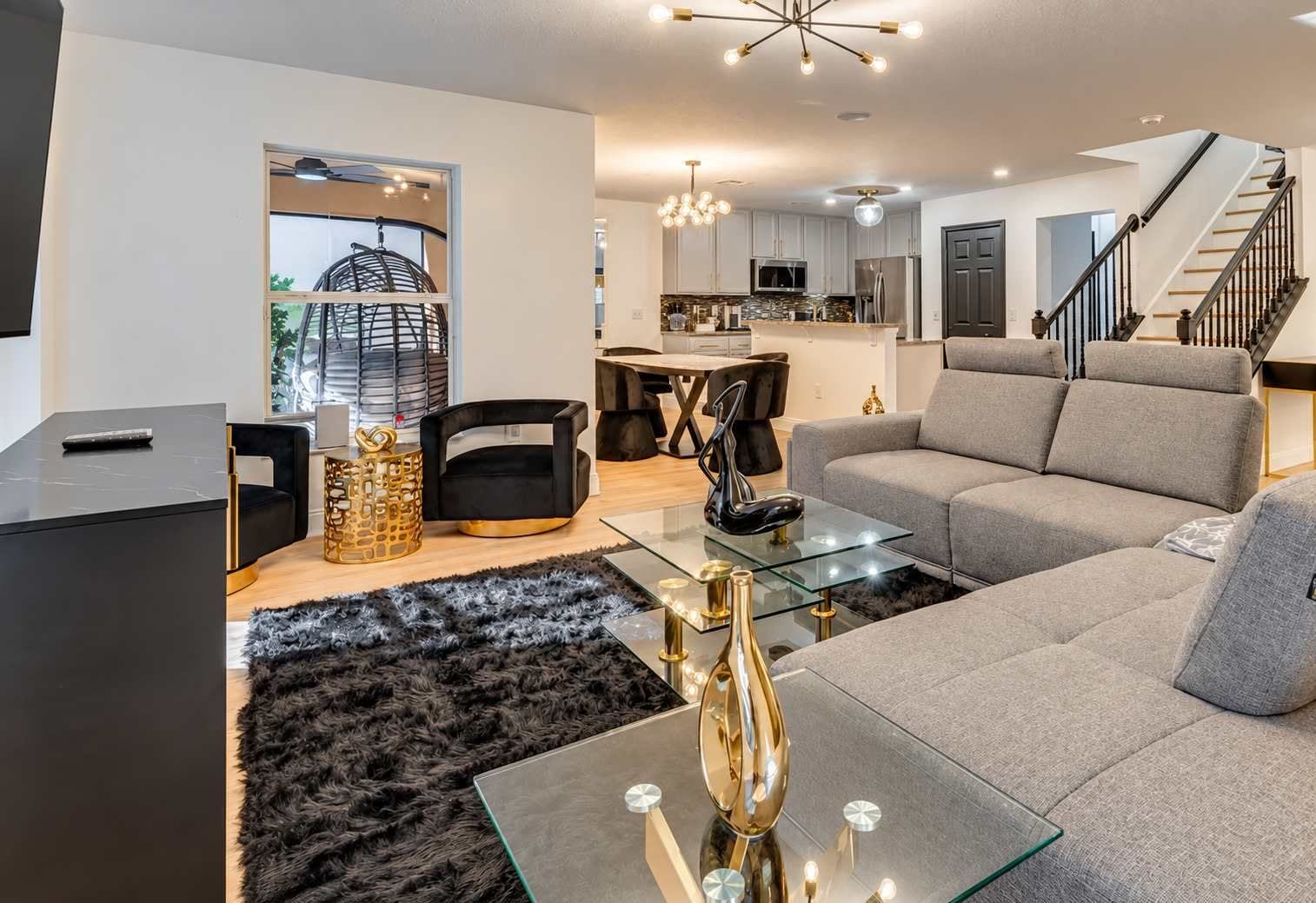 A modern living room with a glass coffee table, a sofa, and a dining area with a chandelier.