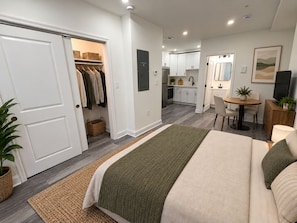 A modern bedroom with a large bed, a walk-in closet, and a kitchenette in the background. - Studio apartment in welcoming Washington with AC and comfort. (Washington)
