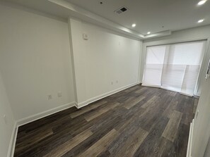 Une pièce dotée d’un plancher en bois, de murs blancs et d’une grande fenêtre avec des stores.