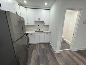 A compact kitchen with white cabinets, a stainless steel refrigerator, and a built-in sink. - Studio apartment in welcoming Washington with AC and comfort. (Washington)