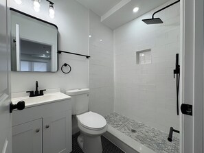Une salle de bain avec des toilettes blanches, un lavabo, un miroir et une douche.