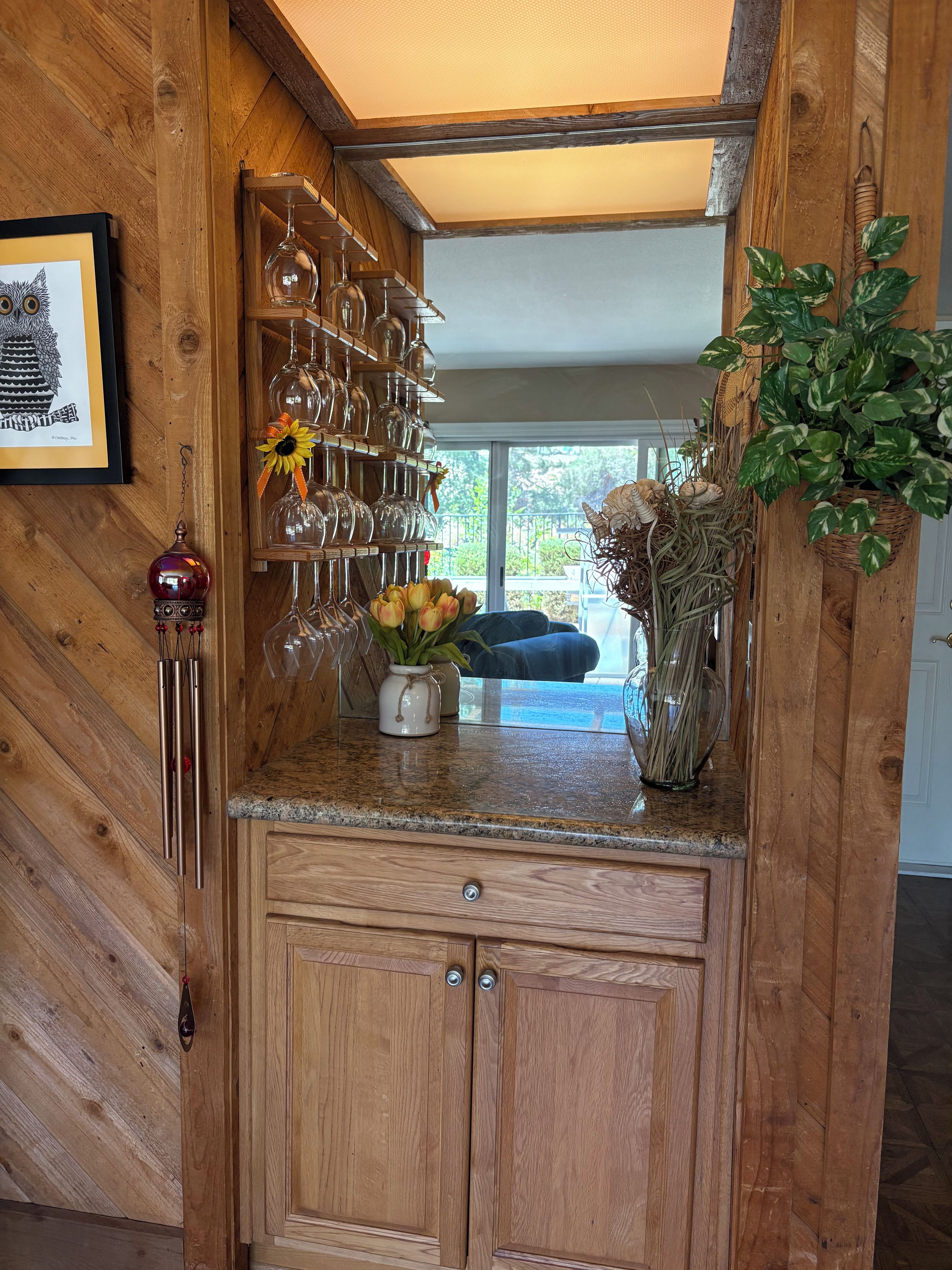 A wooden interior with a glassware rack, a vase with yellow flowers, and a hanging plant.