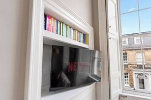 A flat-screen TV mounted on a wall with a bookshelf above it containing various books. - Union | Central 3 Bedrooms | Grand Stay | Sleeps 6 (Edinburgh)