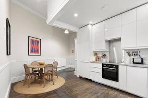 A modern kitchen with white cabinetry, a dining area with a round table and chairs, and a kitchen island with a toaster. - Union | Central 3 Bedrooms | Grand Stay | Sleeps 6 (Edinburgh)
