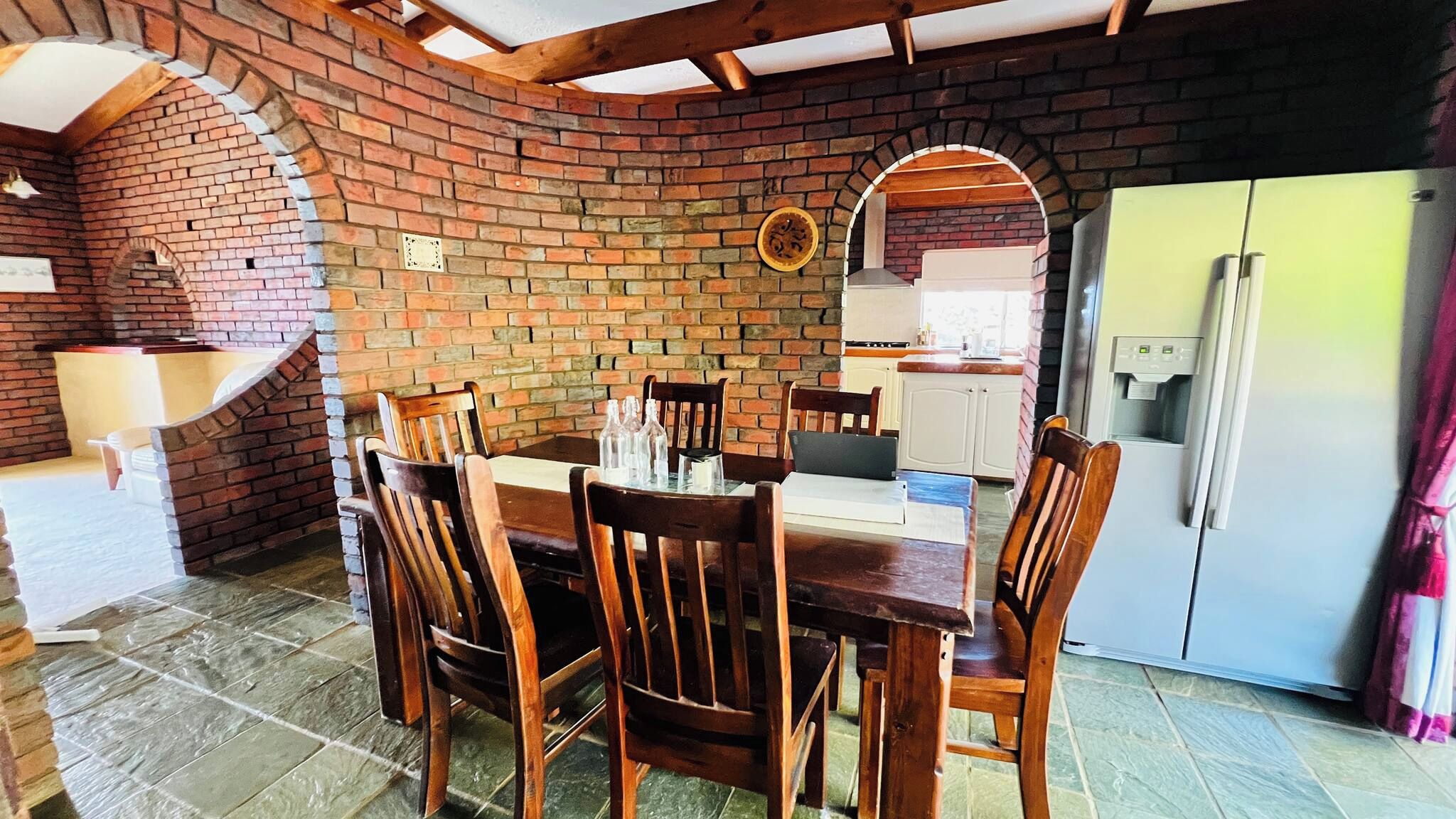 A dining area with a brick wall, wooden chairs, a table, and a refrigerator.