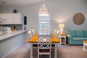 A dining area with a table and chairs, a hanging light fixture, and a window with blinds. - 5 Miles from Sunset Beach with a Pool and Golf Course Views (Sunset Beach)