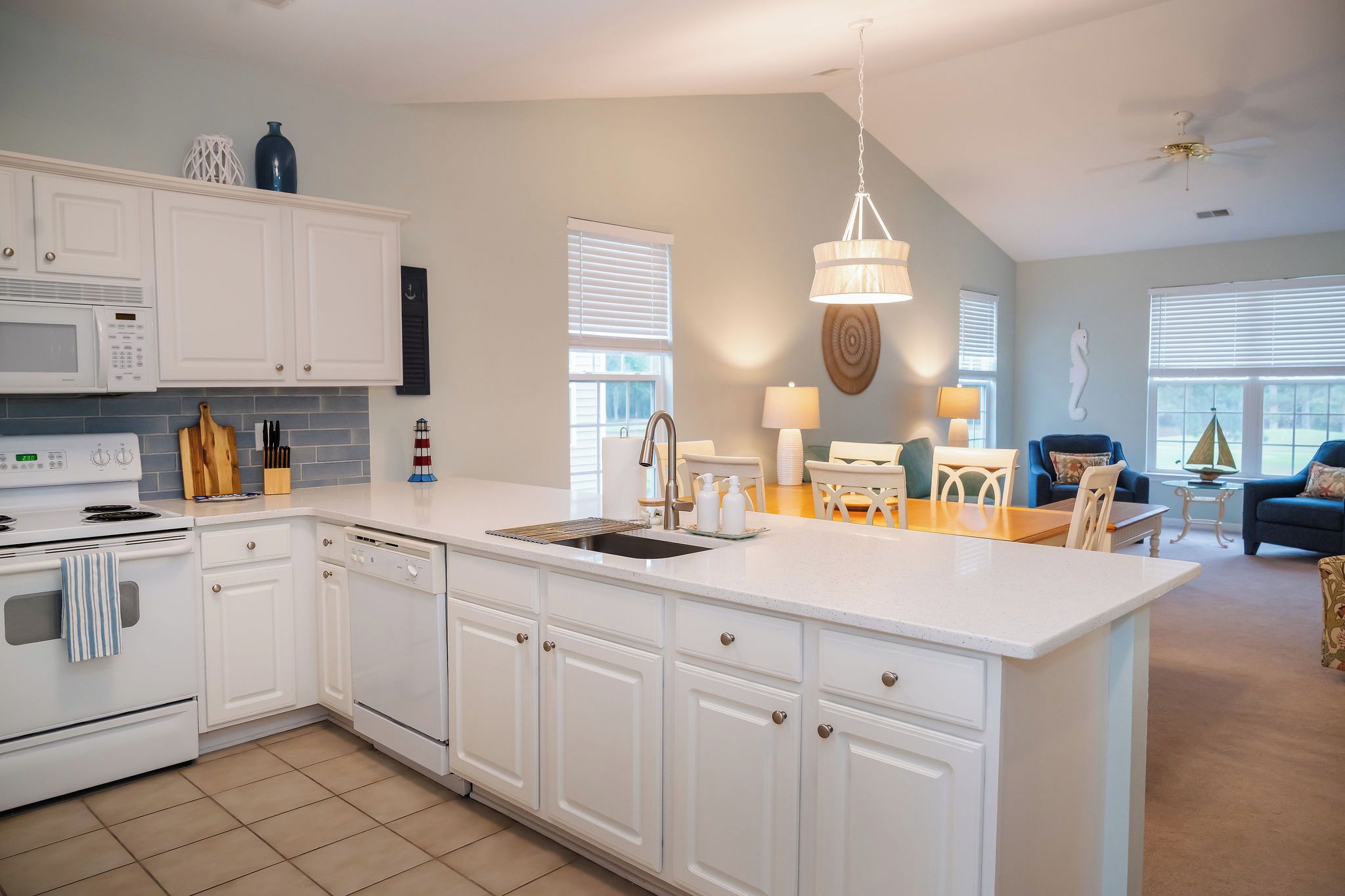 A modern kitchen with white cabinetry, a central island, and a dining area with a blue sofa and table.