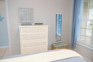 A bedroom with a bed, a white dresser with drawers, a small bench, a wall-mounted mirror, and a window with blinds. - 5 Miles from Sunset Beach with a Pool and Golf Course Views (Sunset Beach)