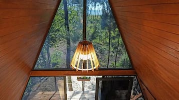 Una habitación de madera con forma triangular, una lámpara colgante y vistas al bosque.