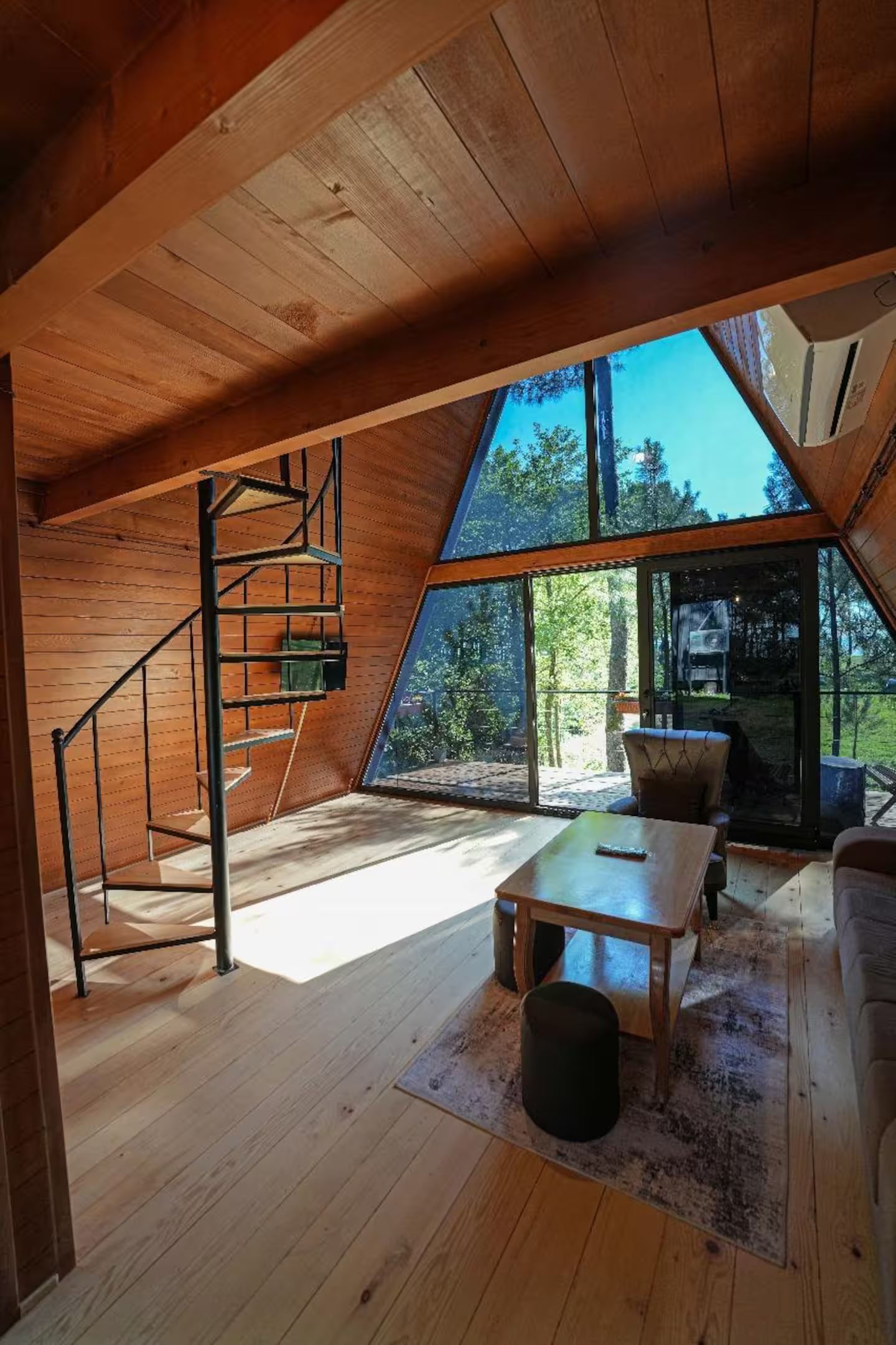 A wooden interior with a sloped ceiling, a wooden staircase, a table, and a chair.