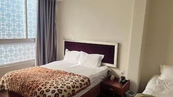 Habitación de hotel con cama, mesita de noche, ventana con cortinas y vista al exterior.