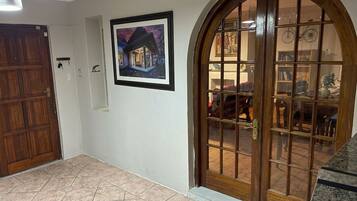 Un pasillo con una puerta de madera, un cuadro enmarcado en la pared y una puerta de cristal que da a una habitación amoblada.