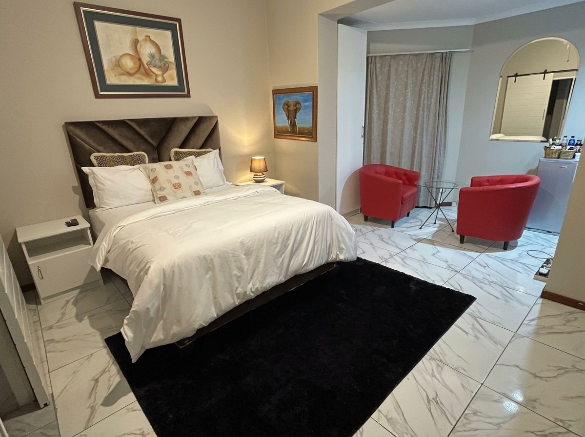 Une chambre d’hôtel avec un lit, une table de chevet, une lampe, une chaise rouge et un miroir.