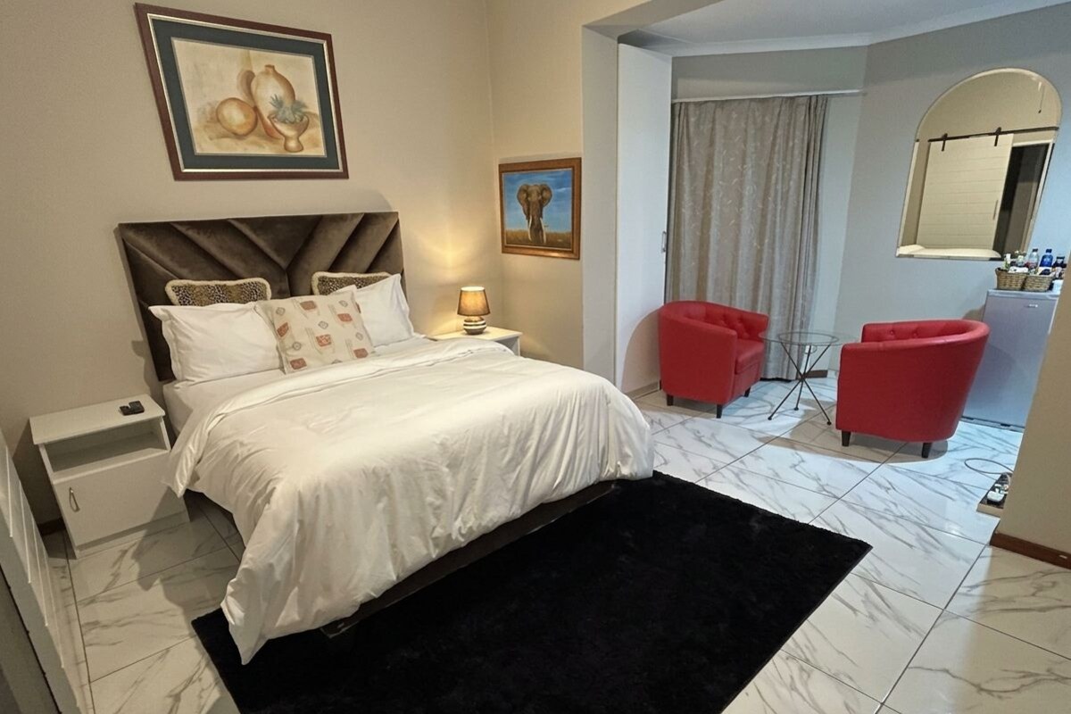 Una habitación de hotel con una cama, una mesita de noche, una lámpara, una silla roja y un espejo.