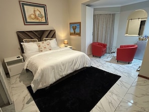 Una habitación de hotel con una cama, una mesita de noche, una lámpara, una silla roja y un espejo.