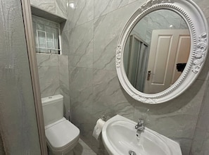 Un baño con inodoro, lavamanos y un espejo grande con marco decorativo.