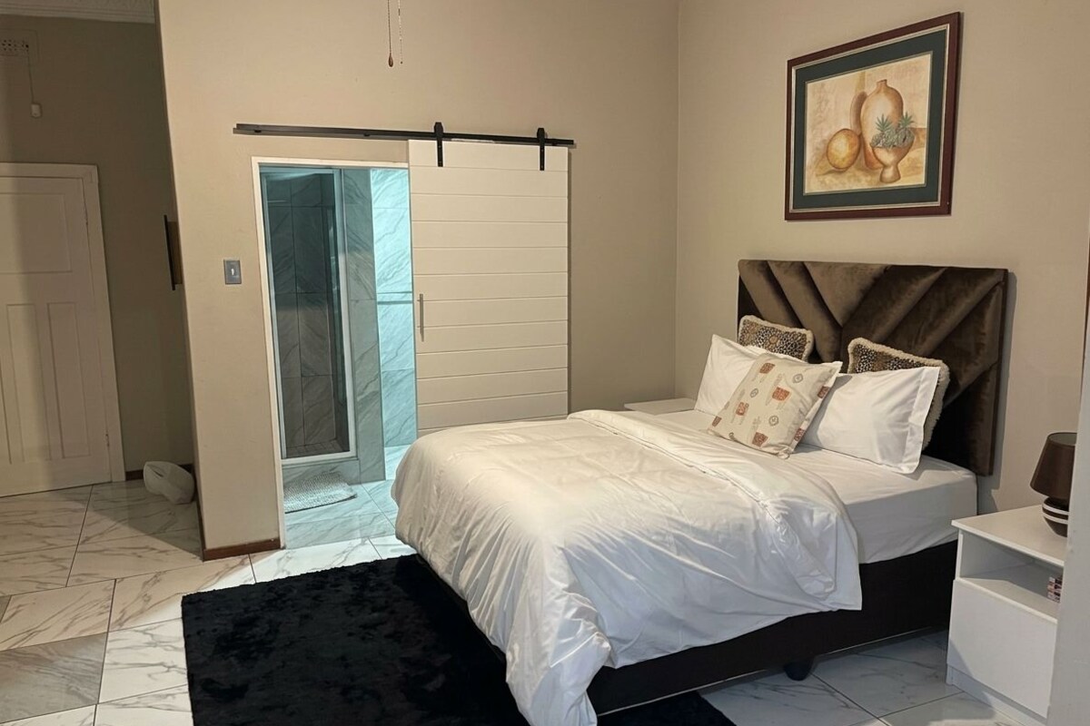 Un dormitorio con una cama, un tapete negro, una puerta blanca y un cuadro en la pared.