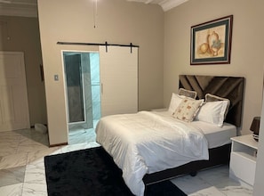 A bedroom with a bed, a black rug, a white door, and a framed picture on the wall.