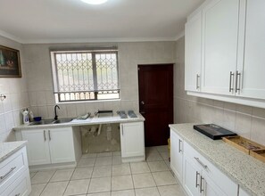 Una cocina con armarios blancos, una ventana con barrotes, un lavamanos y una puerta.