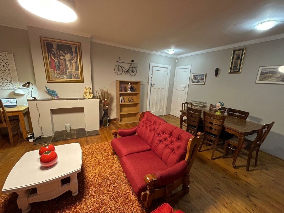 Un salon avec un canapé rouge, une petite table blanche, une table à manger avec des chaises et une cheminée.
