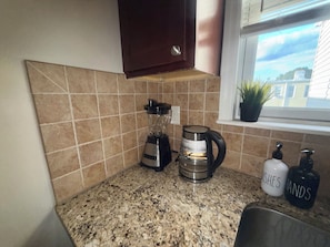 A kitchen with a granite countertop, a blender, a coffee maker, and a window with a view of buildings. - Spacious 3-Bedroom Apartment near New York City! (Harrison)