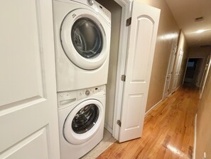 A laundry room with two stacked front-loading washing machines and a white door. - Spacious 3-Bedroom Apartment near New York City! (Harrison)