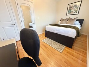 A bedroom with a bed, a chair, a door, and a framed picture on the wall. - Spacious 3-Bedroom Apartment near New York City! (Harrison)